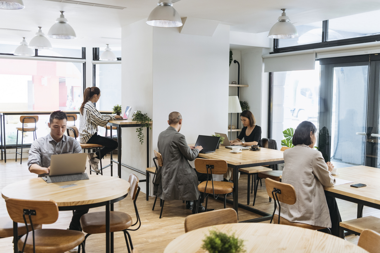 Coworkers sitting at tables independently and using laptops, digital nomad, hot desking, freelancing